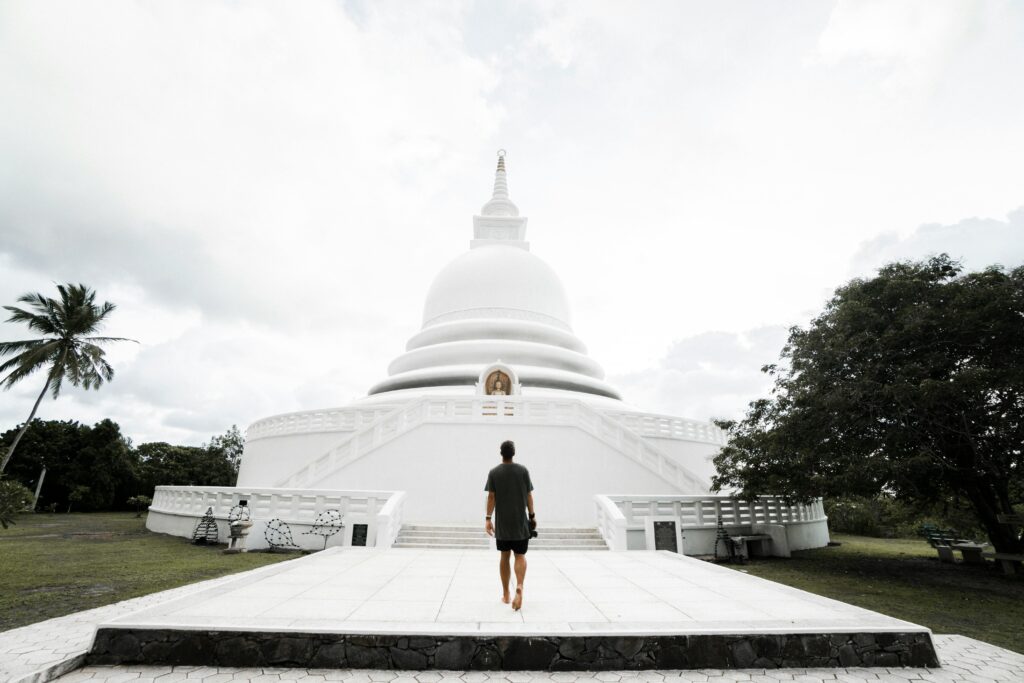 A man walks towards a serene white temple under a cloudy sky, embodying tranquility and exploration.