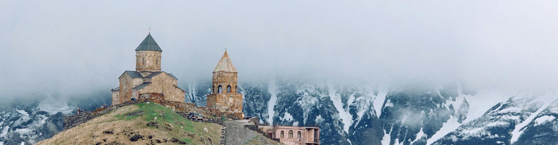 Gergeti Trinity Church atop a hill, shrouded in mist against mountainous backdrop.